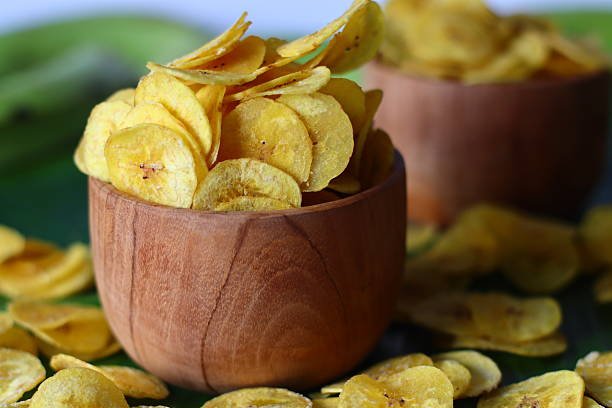 Plantain chips presented in a rustic wooden bowl, featuring thin golden slices. A tropical snack often enjoyed in Kerala, South India. Ideal for themes of tradition, snacking, and regional authenticity